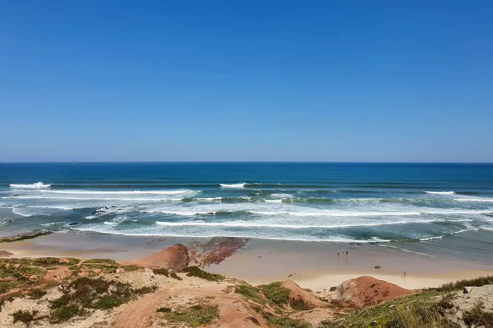 Waves breaking both left and right at the amazing Praia da Almagreira with the red rock formations