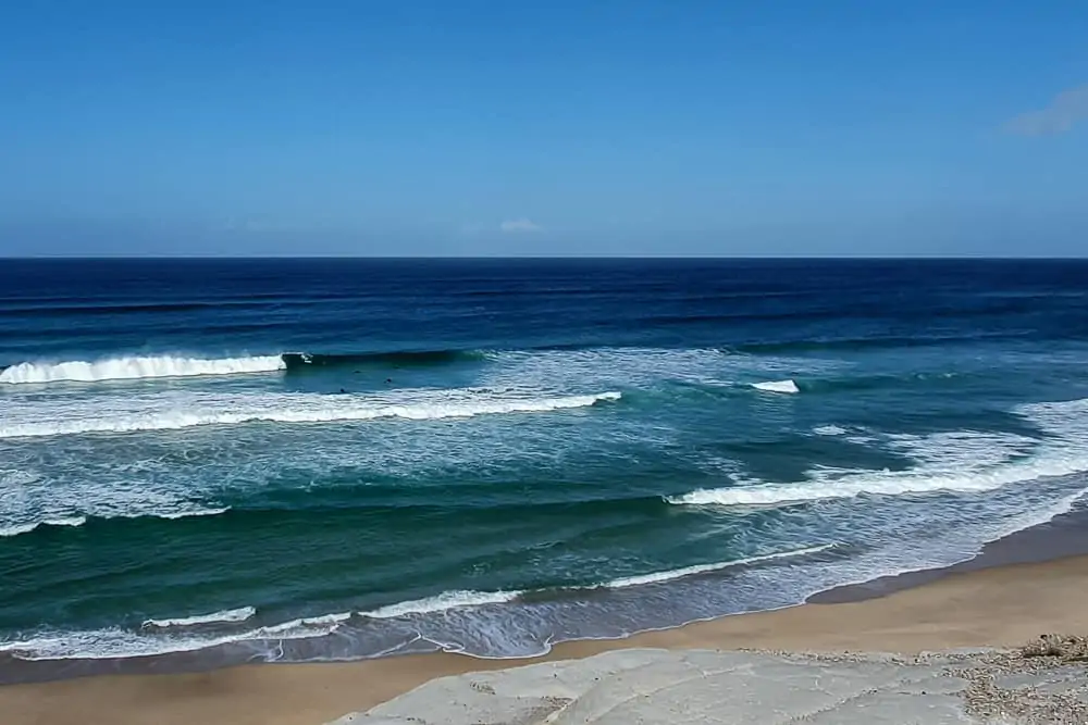 Surfing Praia d'el Rey in front of the light rock formations